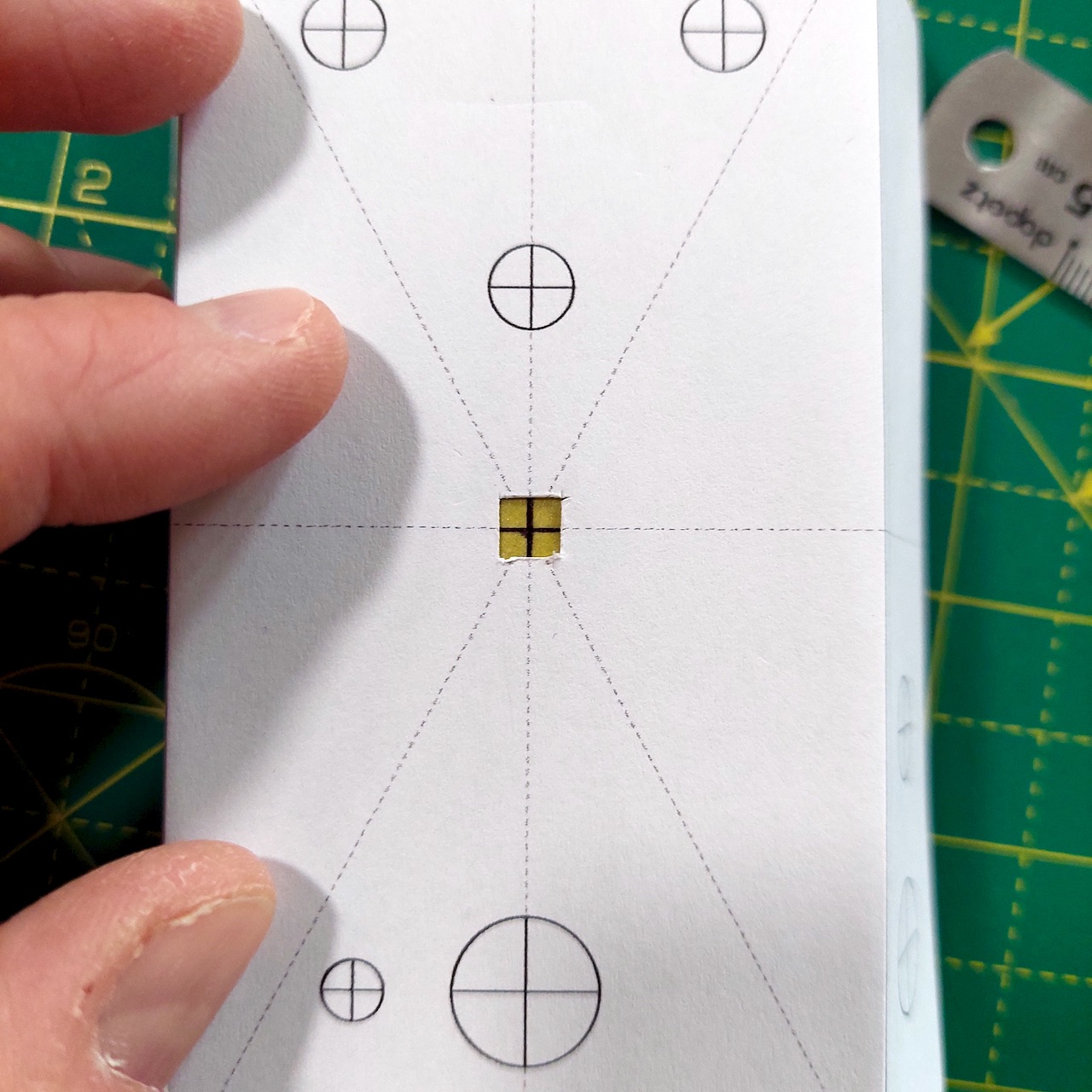 The template held over the enclosure, with the drawn centre cross visible through the cut-out window.