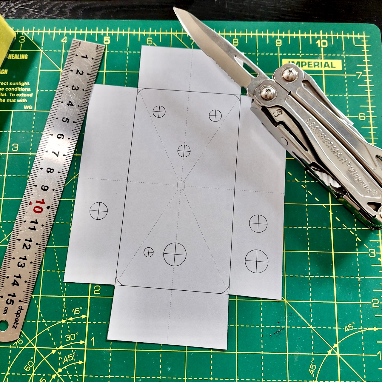 The printed drill template cut out on a cutting mat, with a steel rule and a multi-tool beside it.