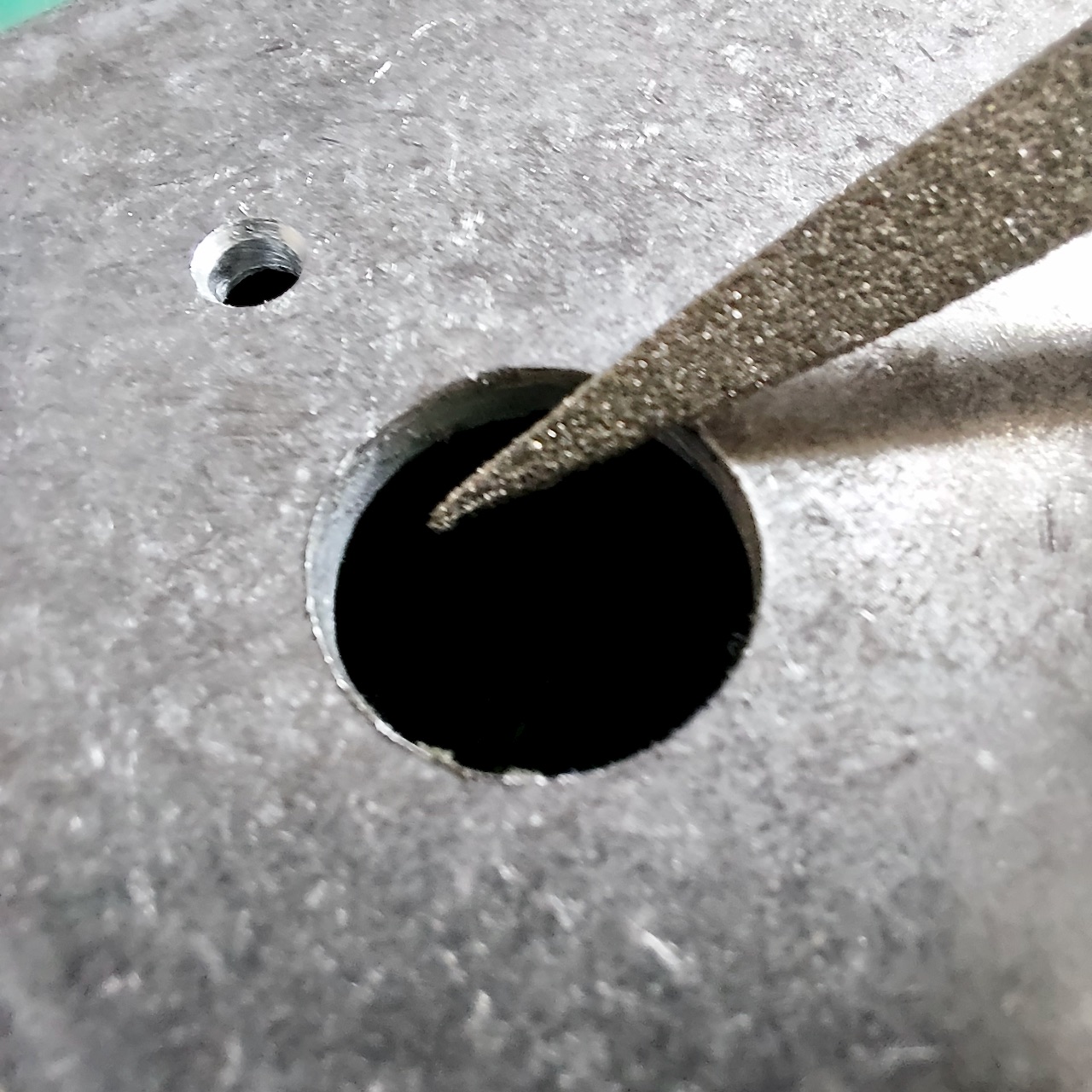 A needle file taking the burr off the edge of a finished hole in a bare aluminium enclosure.