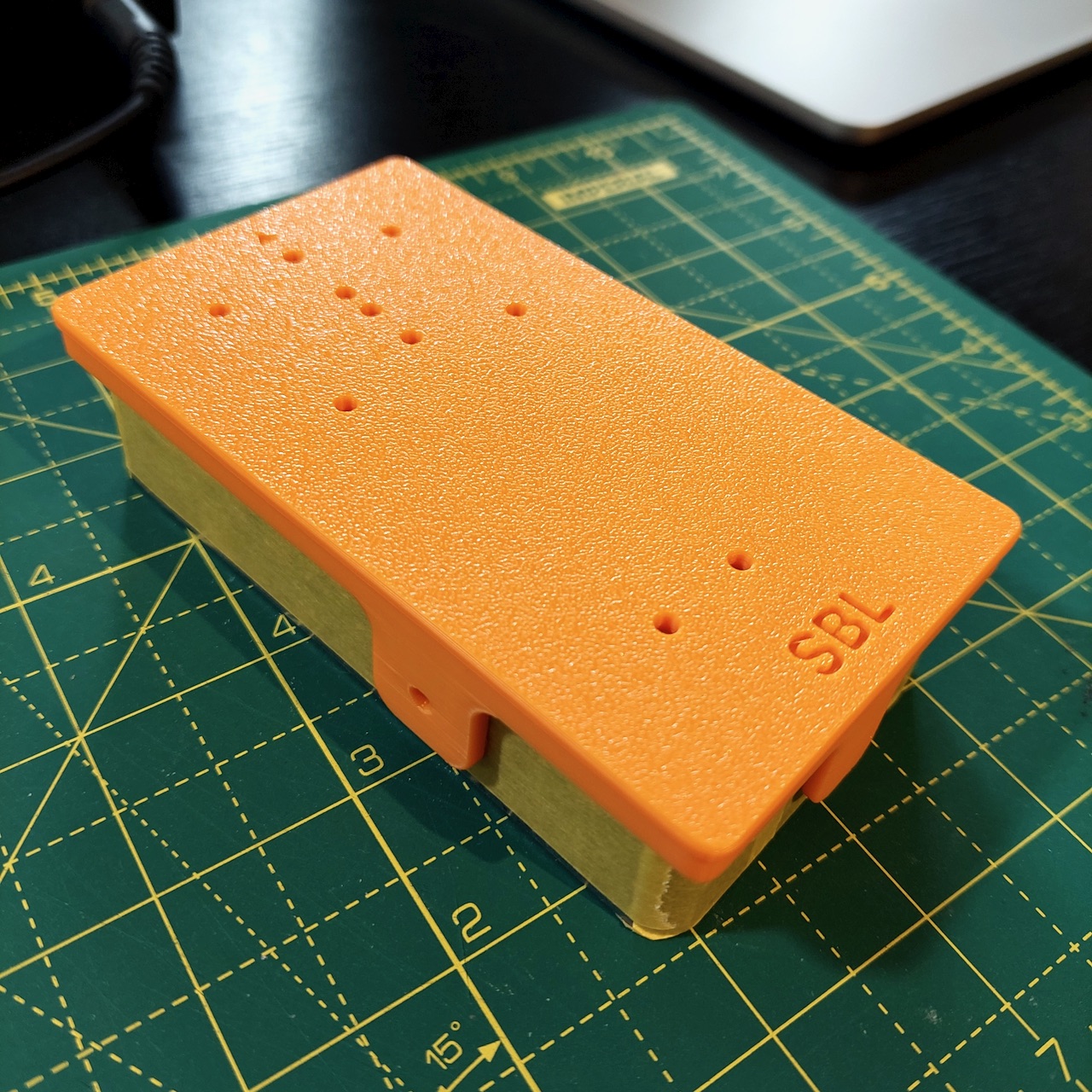 An orange 3D printed drill jig sitting on a masked pedal enclosure, with a hole over every drill position.